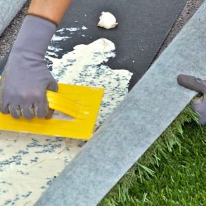 Glue being spread evenly across the underside of turf