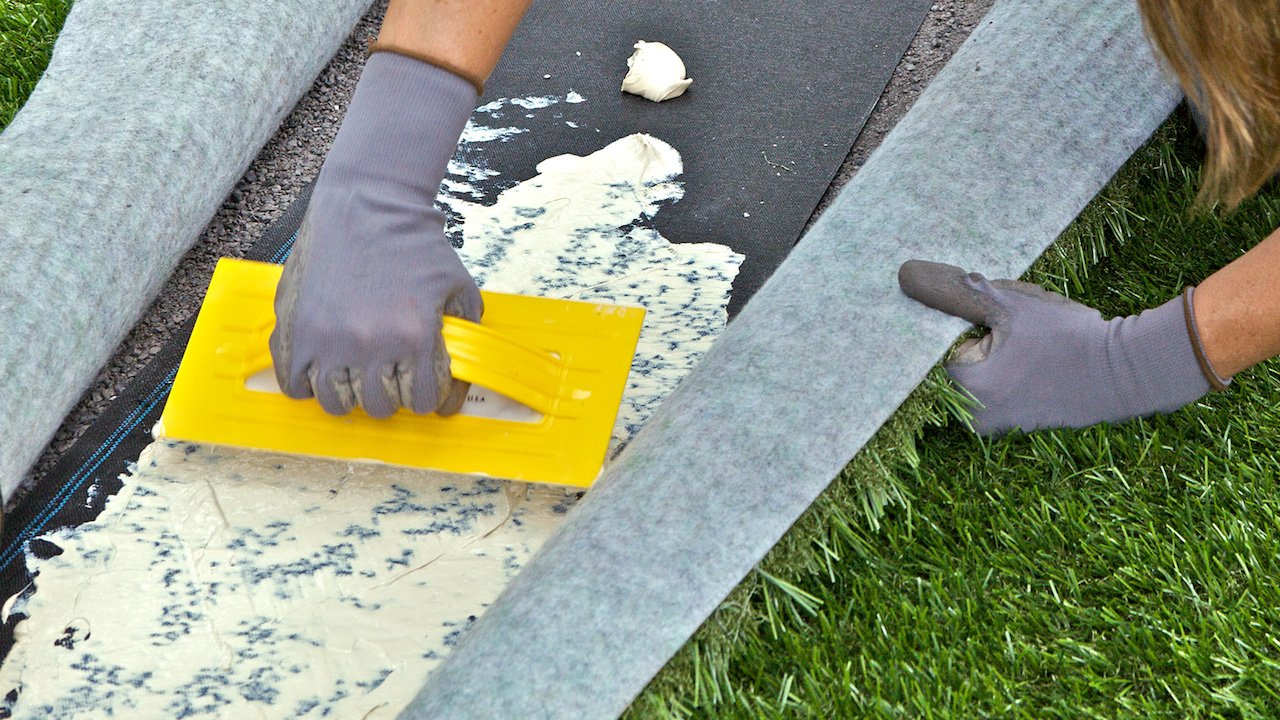 Glue being spread evenly across the underside of turf